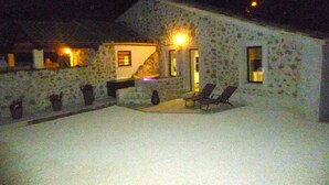 A stone building with a sloped roof, a small porch with two chairs, and a lit window. - Stone house with Jacuzzi and air conditioning (Vallon-Pont-D'arc)