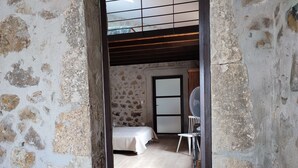 A rustic room with exposed stone walls, a wooden floor, a bed, a chair, and a fan. - Stone house with Jacuzzi and air conditioning (Vallon-Pont-D'arc)