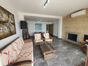 A living room with a sofa, chairs, a coffee table, a fireplace, and a wall-mounted air conditioner.