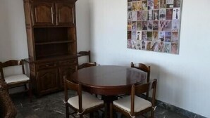 A dining area with a round wooden table and four chairs, a wooden cabinet, and a collage of images on the wall. - ROSES: Super Apartment on the FIRST LINE OF THE SEA for 6–8 PEOPLE in the CITY CENTER (ROSAS)