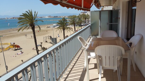 A balcony with a view of the beach, a table with chairs, and a red umbrella. - ROSES: Super Apartment on the FIRST LINE OF THE SEA for 6–8 PEOPLE in the CITY CENTER (ROSAS)
