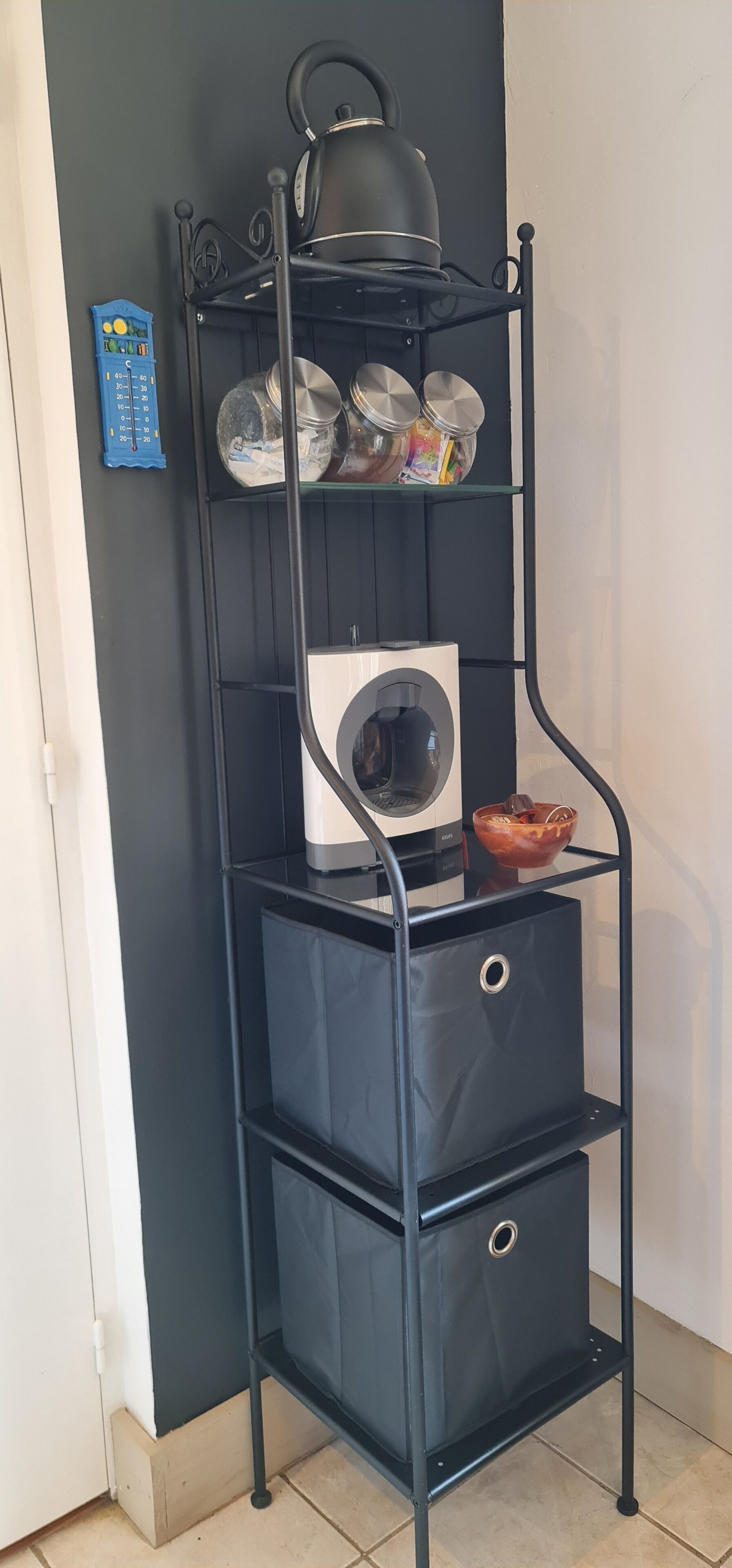 A black metal shelf unit with a washing machine, a kettle, and various kitchen items.