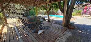 Eine Terrasse im Freien mit Holztisch und -stühlen, umgeben von Bäumen und einem Pool.