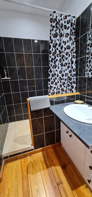 Ein Badezimmer mit Holzboden, einem weißen Waschbecken, einem Spiegel und einer Duschkabine.