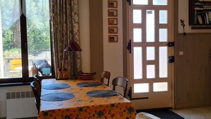 Un coin repas avec une table dressée pour deux personnes, une fenêtre avec des rideaux et une porte dotée de panneaux en verre dépoli.
