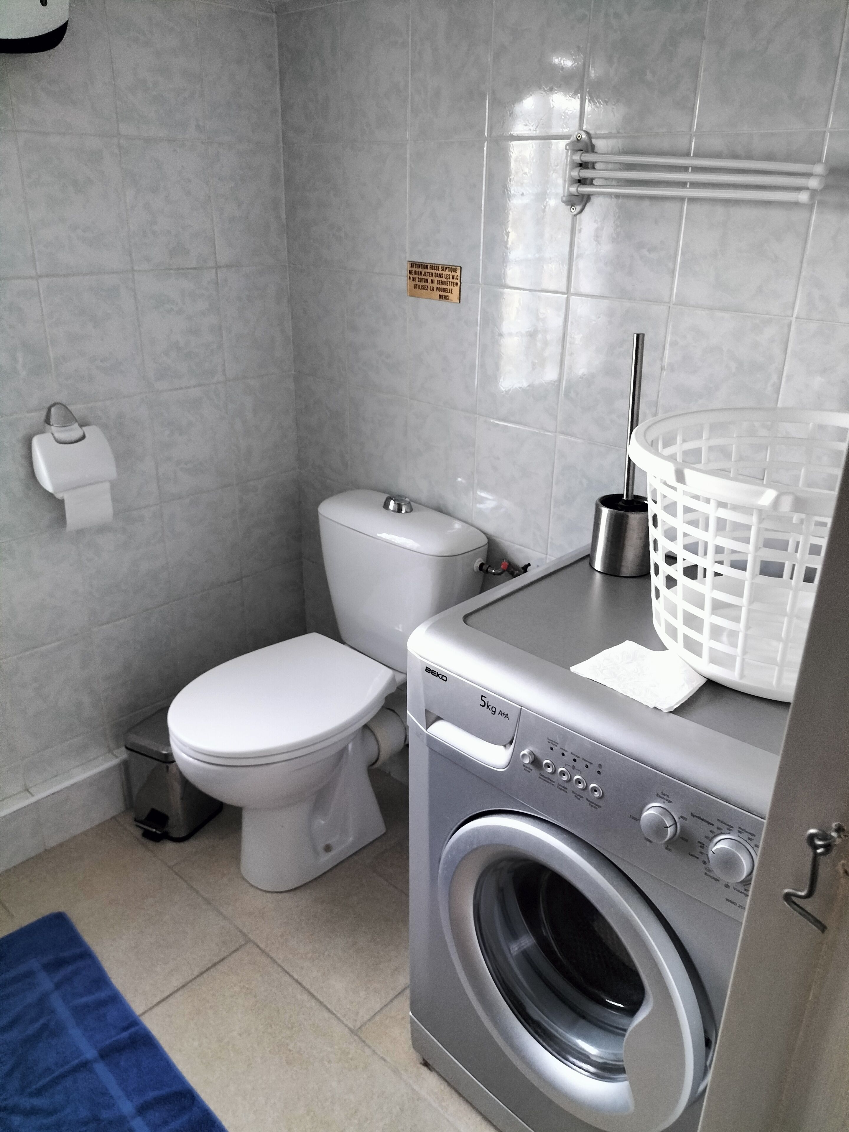 Une petite salle de bain comprenant des toilettes, un lave-linge et un panier à linge.