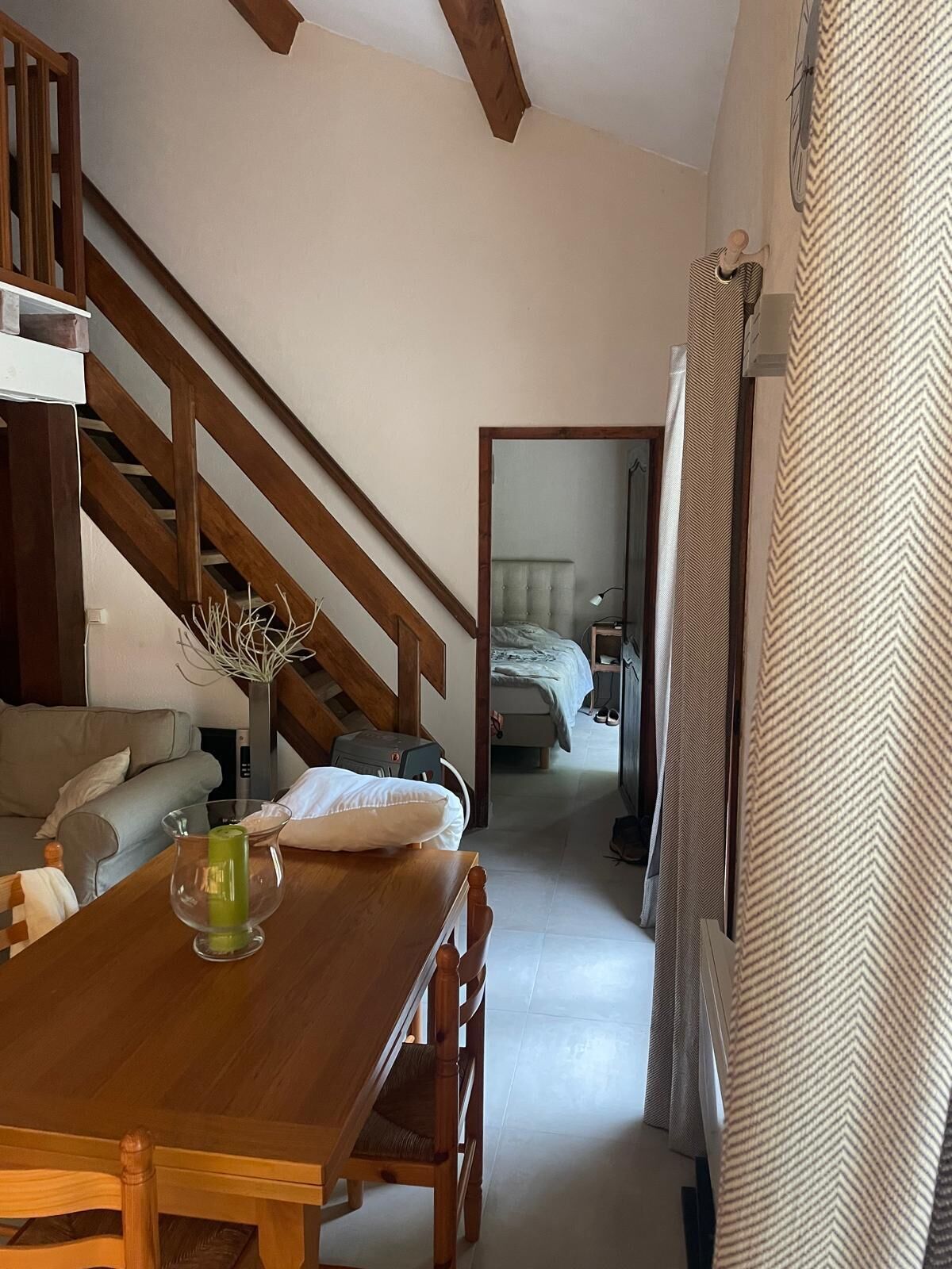 Une pièce chaleureuse avec un escalier en bois, une table à manger avec des chaises, un canapé et un lit avec une tête de lit.
