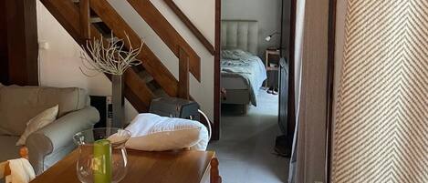Une pièce chaleureuse avec un escalier en bois, une table à manger avec des chaises, un canapé et un lit avec une tête de lit.