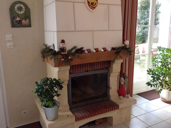 A fireplace with a mantel decorated with pine branches and a snowman figure. There are two potted plants, one on each side of the fireplace.