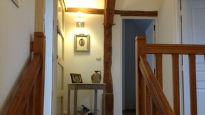Un pasillo con barandillas de madera, una pequeña mesa con un florero y un cuadro enmarcado, y un aplique de pared.