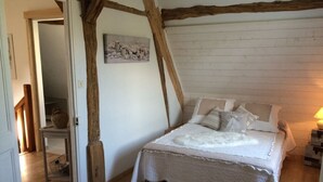 Un dormitorio con techo de madera, una cama con ropa blanca, una mesita con una cesta y un cuadro en la pared.
