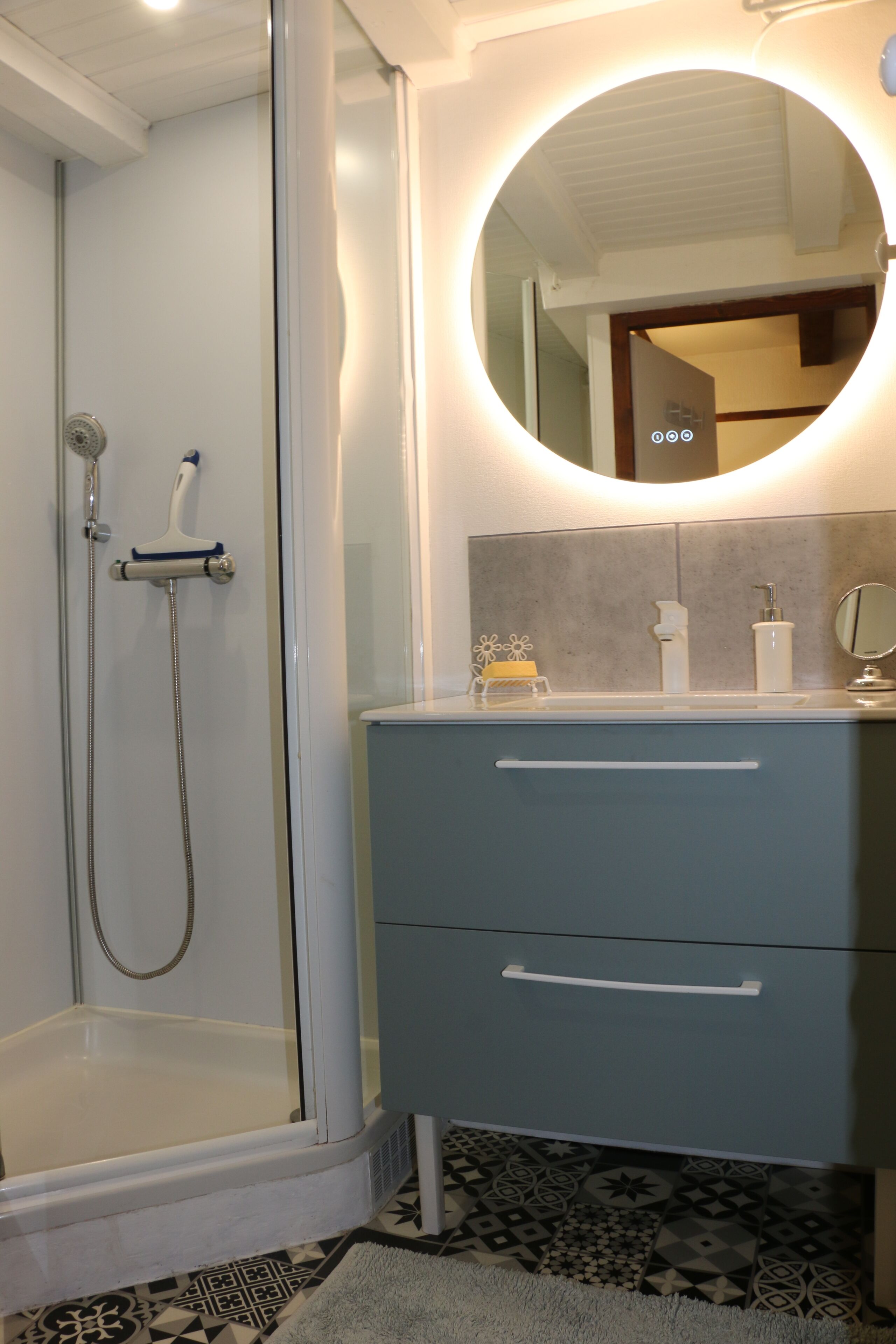 A bathroom with a walk-in shower, a vanity with a mirror, and a patterned floor.