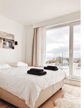 Ein modernes Schlafzimmer mit großem Bett, Blick auf die Stadt durch eine Schiebeglastür und minimalistischer Einrichtung.