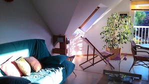 Een gezellige woonkamer met een blauwgroene bank, een houten salontafel en een groot raam met uitzicht op groen.