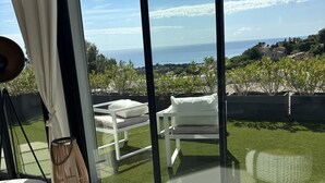 Una habitación moderna con un gran ventanal que da a un balcón con vistas al mar y al verdor.