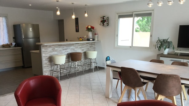 A modern kitchen with a refrigerator, a dining area with a table and chairs, and a bar with stools.