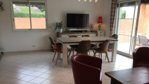A spacious living area with a dining table, chairs, a television, and a sliding glass door to the outside.