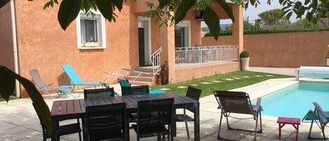 A patio with a pool, outdoor seating, and a house with a balcony.