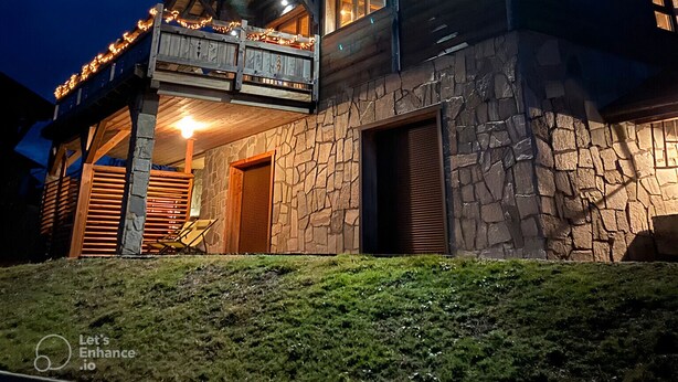 Eine zweistöckige Blockhütte mit Steinverkleidung, einem Balkon mit Lichterketten und einer Holzterrasse.