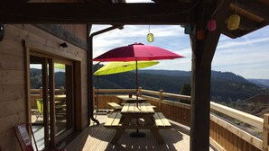 Eine Holzterrasse mit Picknicktischen und einem Sonnenschirm mit Blick auf eine gebirgige Landschaft.