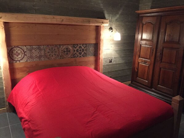 Une chambre avec un lit, une tête de lit en bois, un mur décoré d’un motif et une armoire.