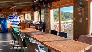 Ein rustikales Holzinnenambiente mit einem langen Tisch, Stühlen, einem Herd und Blick ins Freie.
