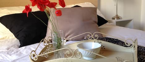 Un lit sur lequel se trouve un plateau portant un vase avec des fleurs rouges, une tasse blanche et un plateau décoratif orné de motifs floraux.