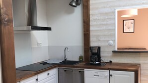 A compact kitchen with white cabinetry, a built-in dishwasher, and a wooden beam ceiling.