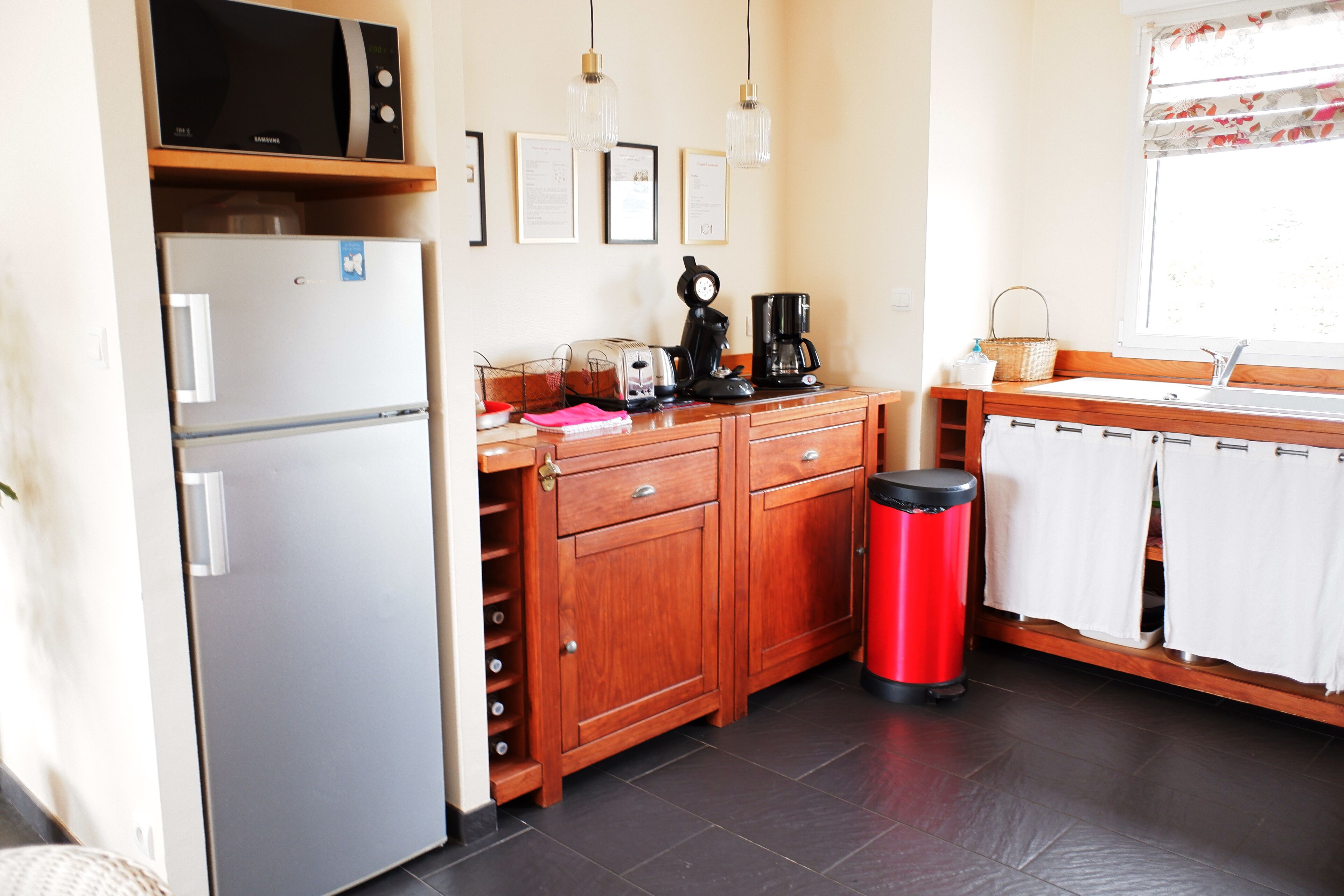Een praktische keuken met een koelkast, magnetron, broodrooster, koffiezetapparaat en een rode prullenbak.