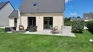 Une maison moderne dotée d’un patio aménagé avec du mobilier d’extérieur, une porte-fenêtre coulissante et une pelouse bien entretenue.