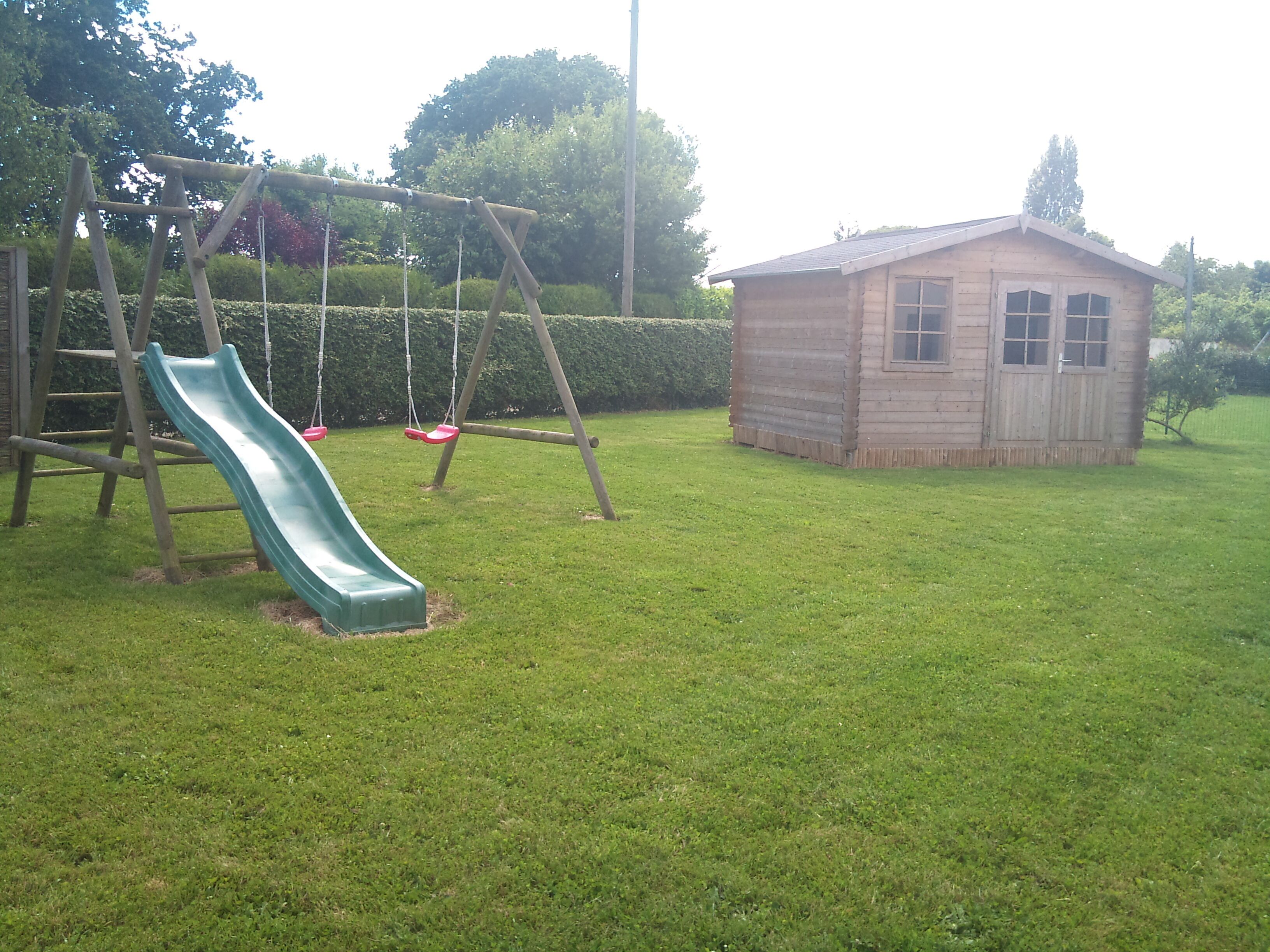 A playground with a slide and swings, a wooden shed, and a well-maintained lawn.