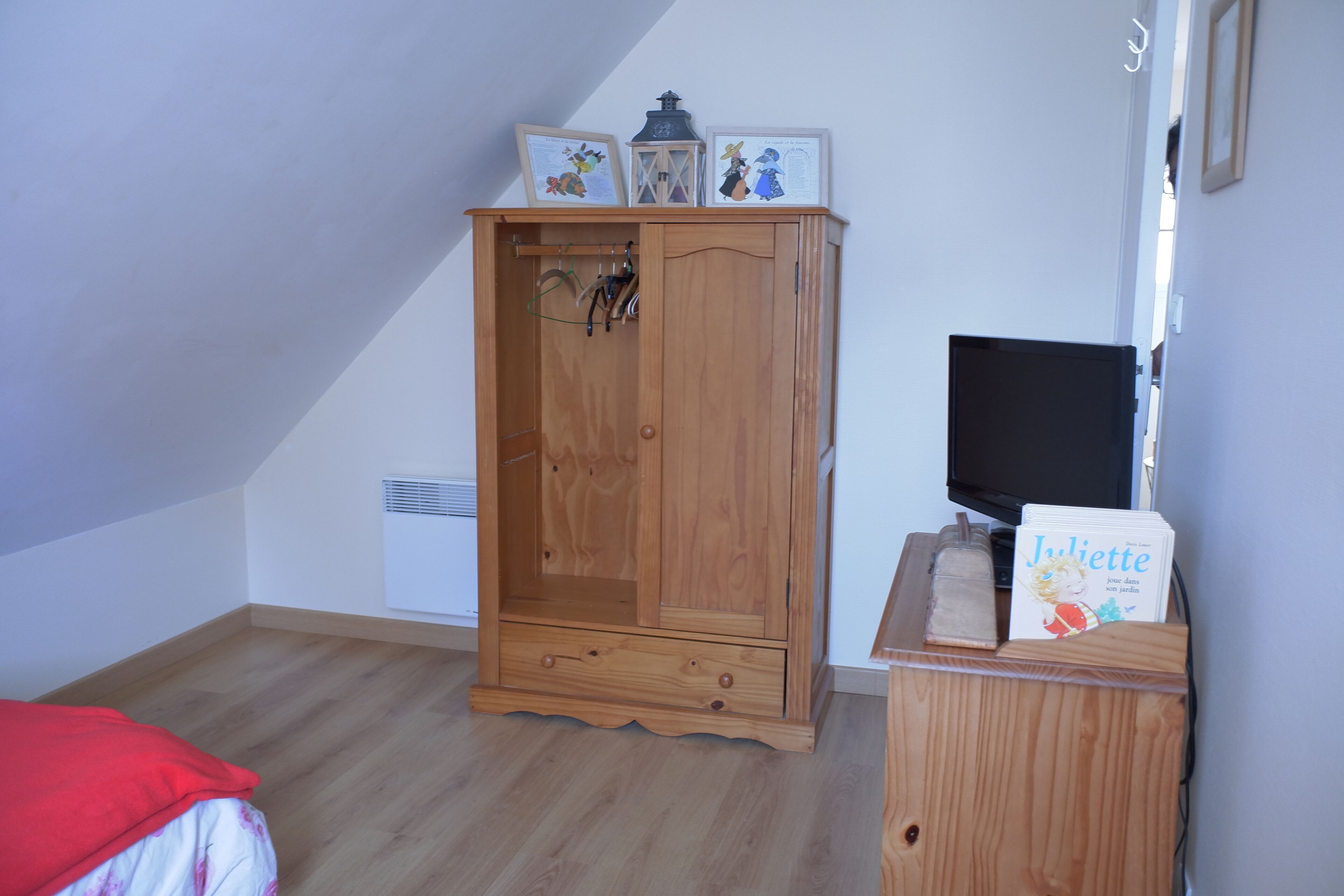 A room with a wooden wardrobe, a television, and a book on a small table.