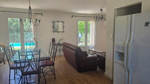 Ein Essbereich mit einem Glastisch, Stühlen, einem braunen Sofa und einem weißen Kühlschrank.