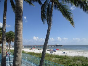 A beach with palm trees, a pier, and beach umbrellas.