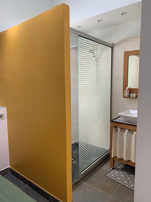 A modern bathroom with a glass shower enclosure, a wooden vanity with a white sink, and a tiled floor.