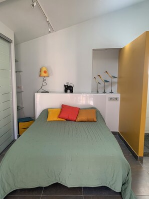 A bedroom with a green bedspread, a small bedside table with a lamp, and decorative items including a cat figurine and bird sculptures.