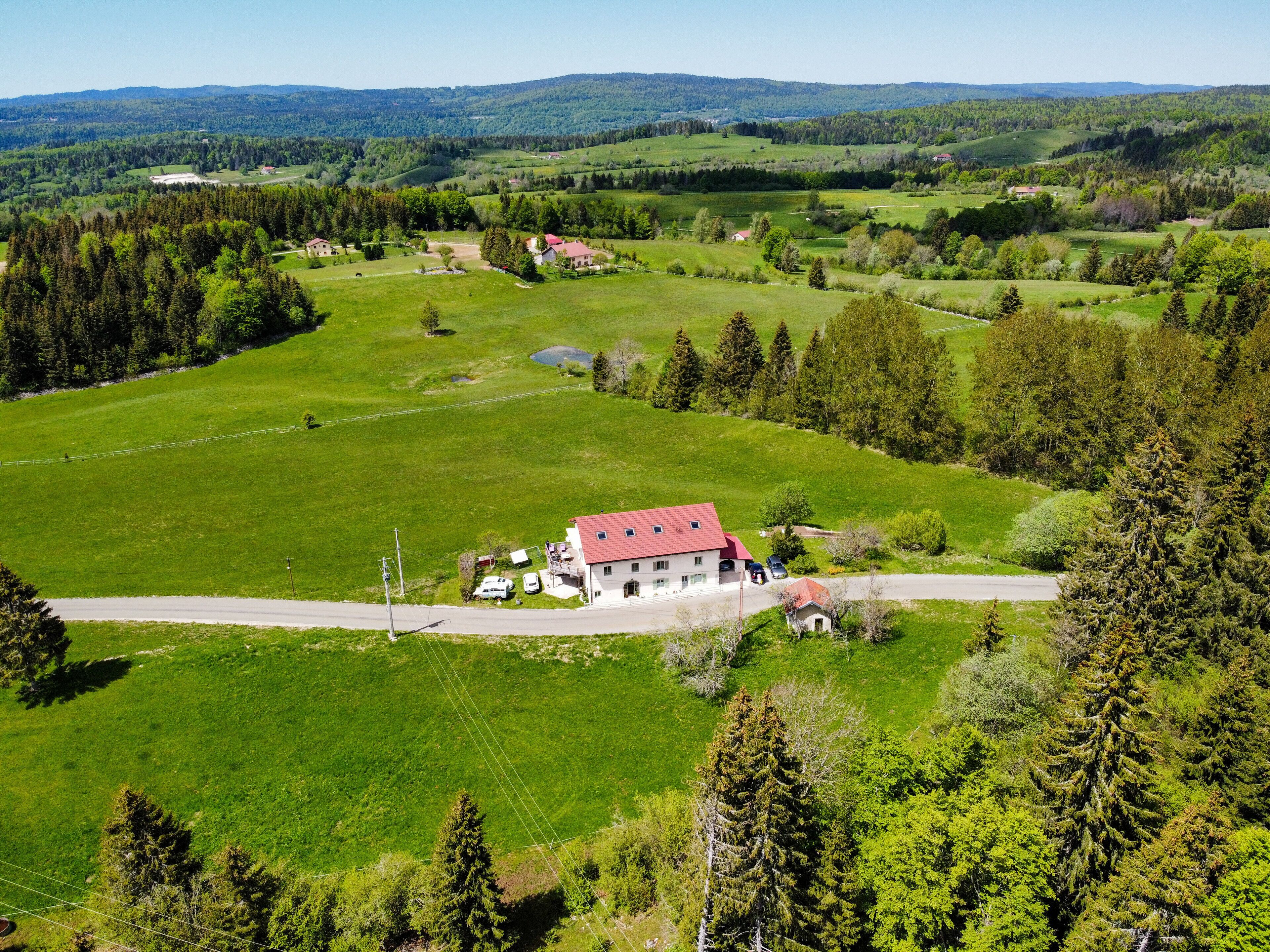 A rural house with a red roof, surrounded by green fields and trees.