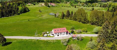A rural house with a red roof, surrounded by green fields and trees.