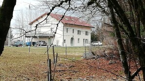 A large, single-story building with a red-tiled roof, surrounded by a grassy area and trees. - Accommodation located at 1000 meters in the countryside (Longchaumois)