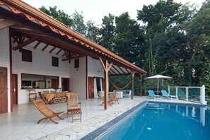 A poolside area with a covered patio, lounge chairs, and a dining table. - Villa Mahagony (Deshaies)