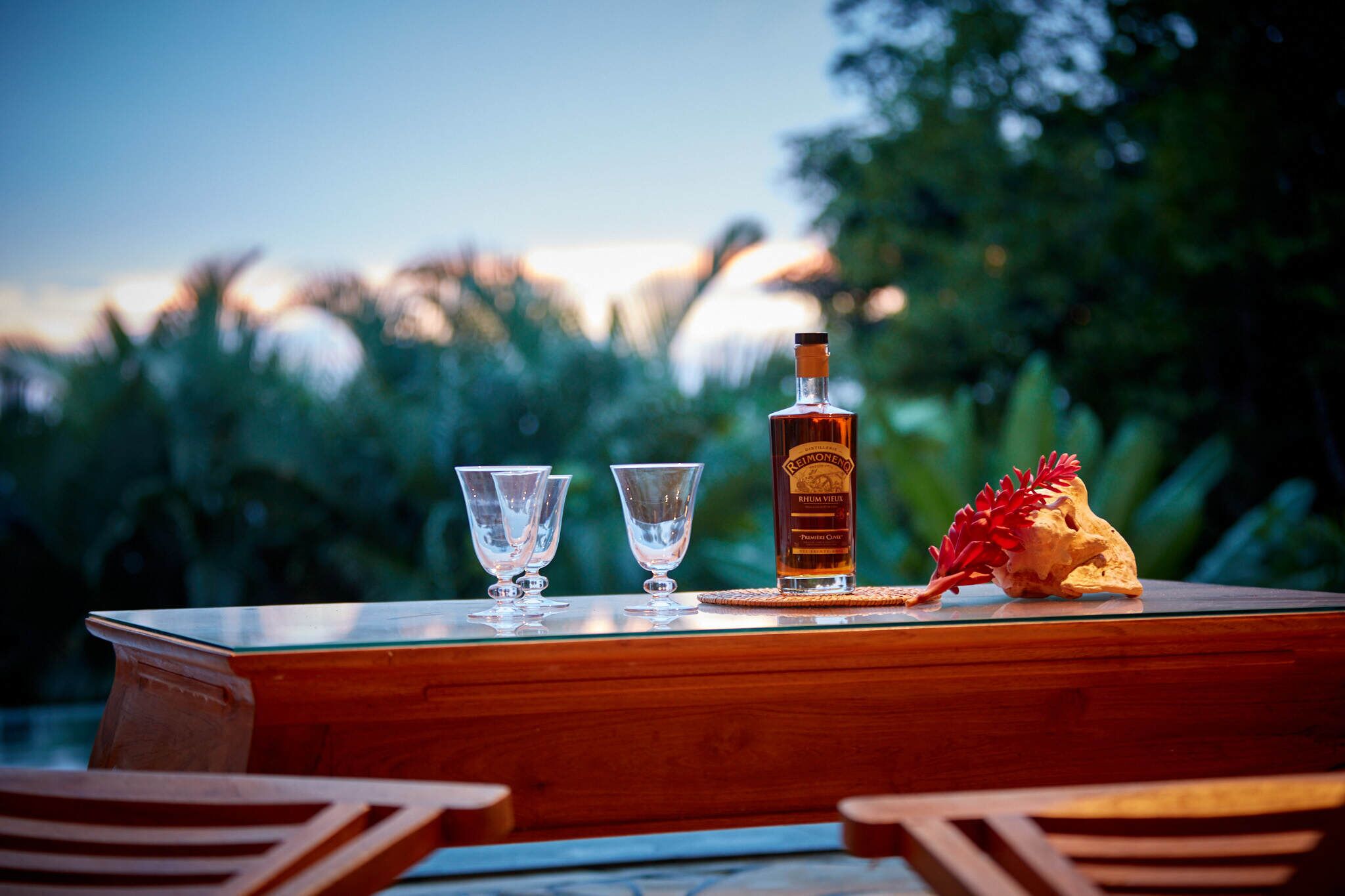 A wooden table with a bottle of liquor, two glasses, and a decorative item.