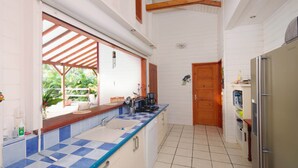 Una cocina con salpicadero de azulejos blancos y azules en damero, vigas de madera en el techo, un refrigerador de acero inoxidable y una ventana con vistas a la vegetación.