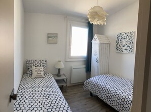 A bedroom with two beds, a window, a lamp, and a wall clock. - My house, feet in the water ... (Saint-Gilles-Croix-De-Vie)
