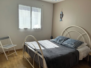 Un dormitorio con cama, una silla, un ventanal y una decoración en la pared.