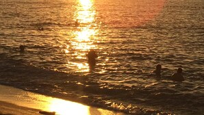Ein Sonnenuntergang über dem Wasser, einige Personen sind darin unterwegs.