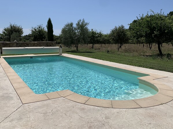 Une piscine rectangulaire, bordée d’une terrasse carrelée, entourée d’une pelouse et d’arbres.