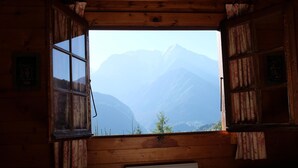 Ein Holzhüttenraum mit einem Bett, einem Fenster mit Vorhängen und einem kleinen weißen Gerät.