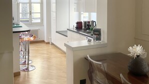 Una cocina moderna con armarios blancos, una isla central y un comedor con una mesa y sillas.