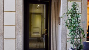 Entrada de un edificio con una puerta negra, un escalón que lleva a ella y una planta en maceta a la derecha.
