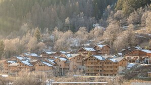 A cluster of wooden cabins with multiple balconies, set against a backdrop of snow-covered trees and a mountainous landscape. - Superb 70M2 apartment, fireplace, terrace, pool/spa and private shuttle service  (Champagny-En-Vanoise)